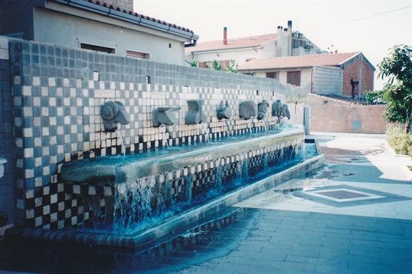 Public fountain with stone spouts, water flowing over white and blue mosaic