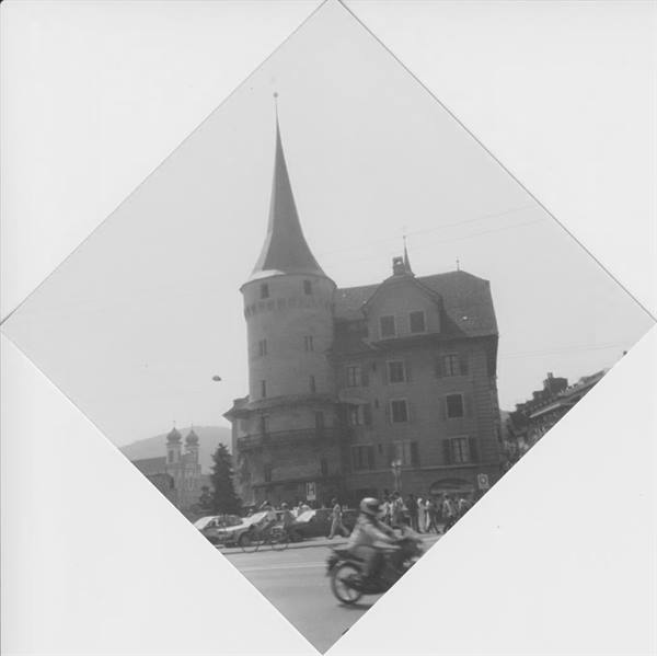 Motorcyclist passing an old spired tower among historic buildings, black and white photo