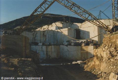 Open-air marble quarry with lattice crane among white blocks, Carrara hills