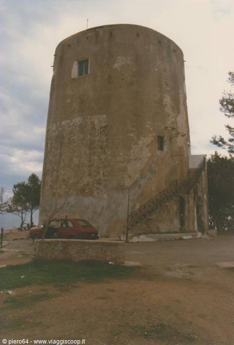 Old cylindrical plastered stone tower with external staircase, car parked below