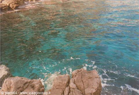 Clear turquoise water between pink rocks, wave foam on the stone