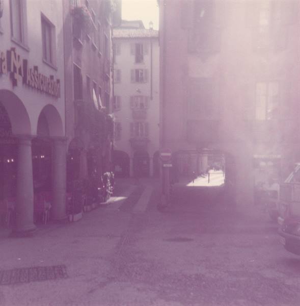 Arcaded street with old buildings, strong sunlight filtering between facades