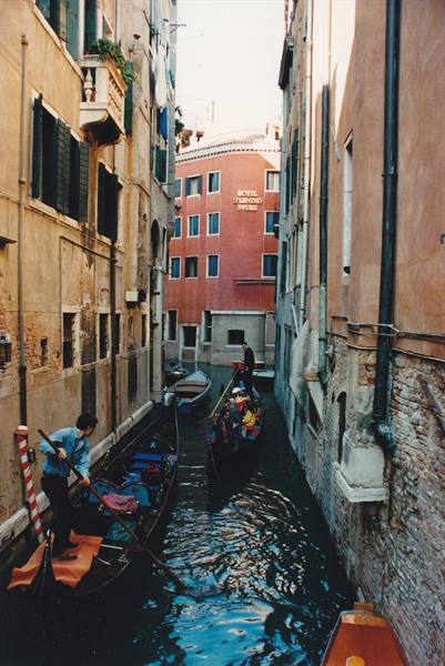 Gondoliers navigating narrow canals between old buildings in Venice