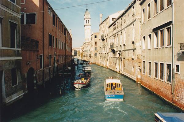 Boats on a Venice canal between old buildings and a sunlit bell tower