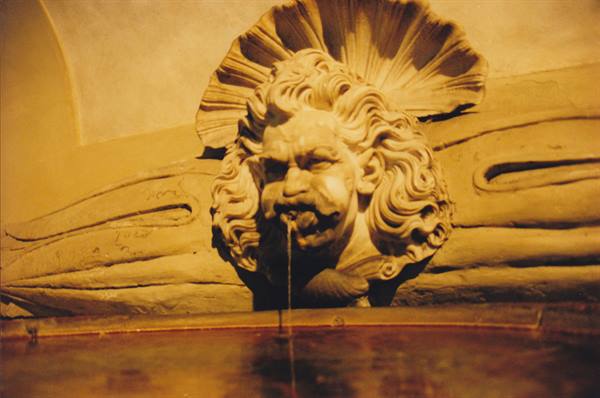 Stone fountain with baroque mascaron spouting water into the basin