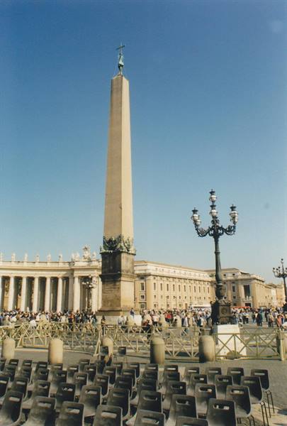 Egyptian obelisk in St. Peter's Square, rows of chairs and crowd under blue sky