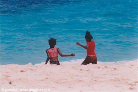 Two girls playing on white sand beach, turquoise sea behind them