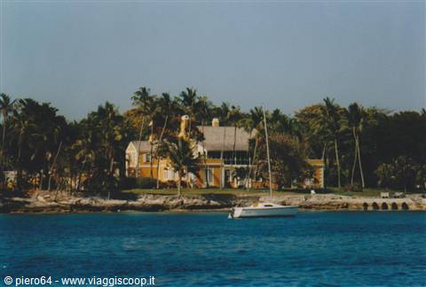 Yellow villa among palm trees by the sea, sailboat anchored in the bay