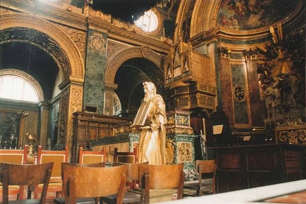 Gilded statue inside a baroque church rich with marbles, carvings and columns