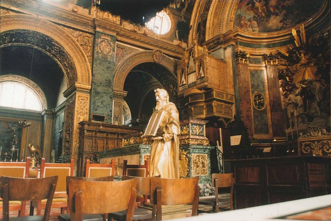 Statua dorata all'interno di una chiesa barocca ricca di marmi, intagli e colonne