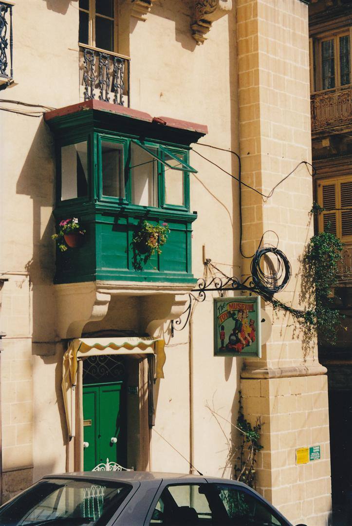 Balcone tradizionale maltese in legno verde su facciata calcarea, con insegna del pub