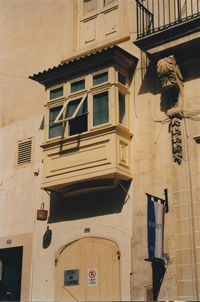 Traditional Maltese enclosed wooden balcony on limestone facade in sunlight
