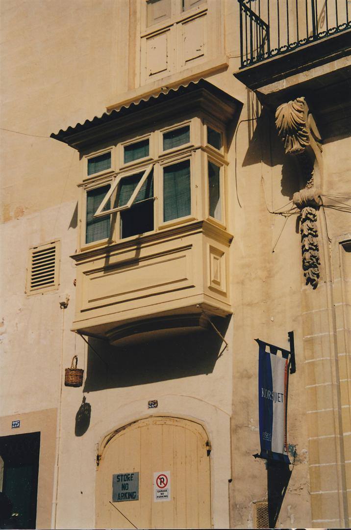 Balcone ligneo maltese chiuso da vetri su facciata in calcare, luce solare