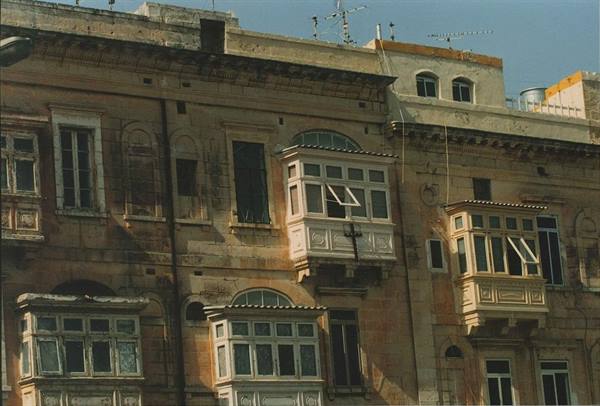 Limestone facade with enclosed wooden balconies under bright sunlight