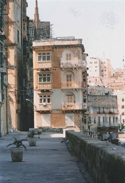 Ochre limestone building with balconies above paved walkway, Valletta