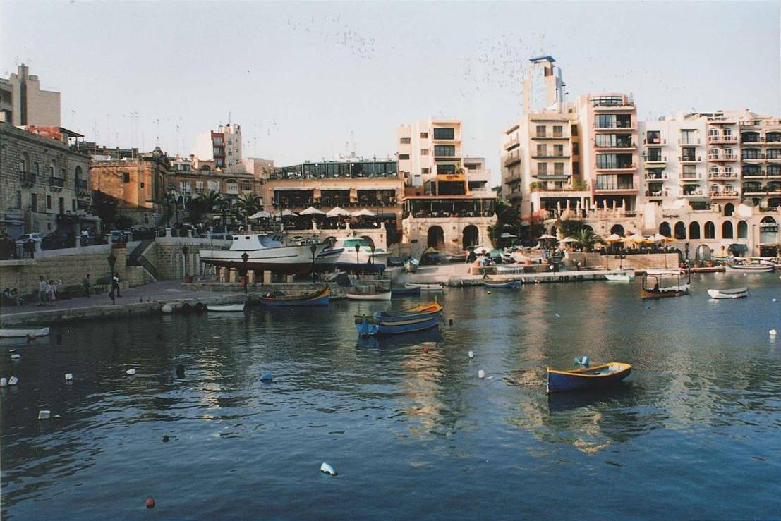Barche colorate ancorate nella baia di Spinola, edifici e ristoranti sul lungomare