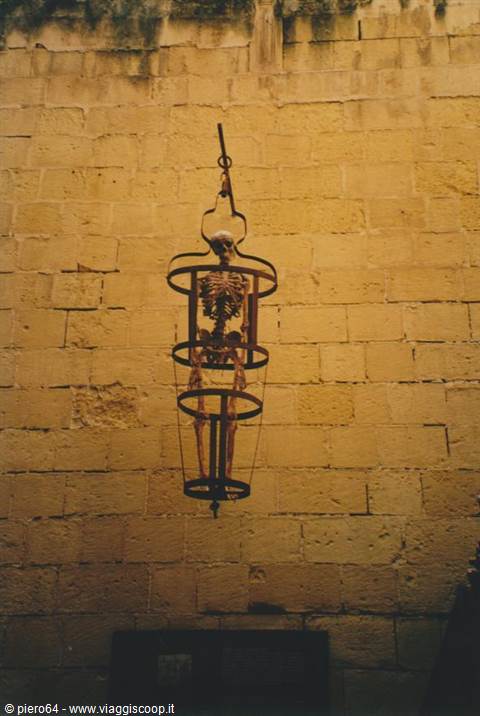 skeleton hanging in iron gibbet cage against yellow stone wall