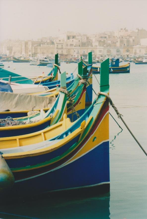 Luzzu dipinti di giallo e blu ormeggiati a Marsaxlokk, luce morbida sull'acqua