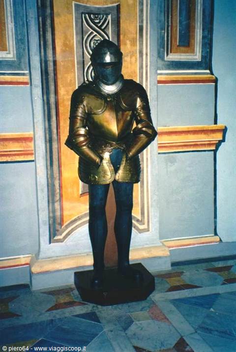 Shining medieval steel armor displayed on a wooden base, frescoed walls