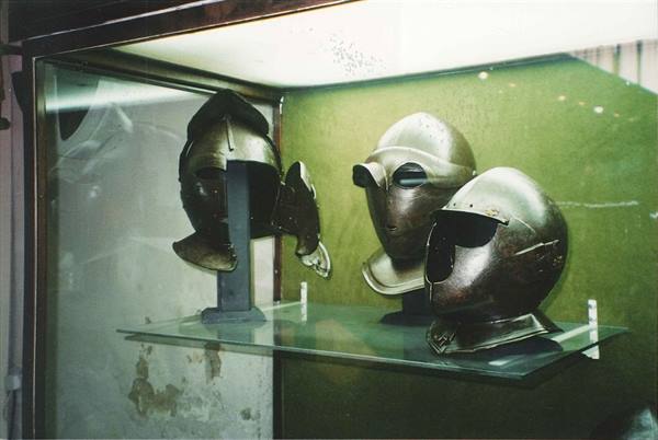 Ancient metal helmets displayed in a museum glass case under artificial light