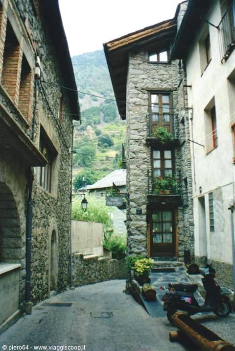 Alley with stone houses, balconies with plants, parked scooter, green mountain behind