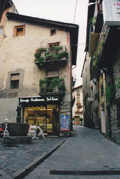 Cobbled alley with stone fountain and pastry shop under flowered balconies