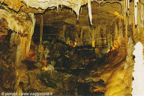 Cave with lit stalactites and stalagmites, metal walkway winding through formations