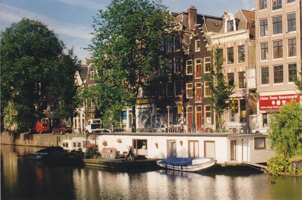 Canal houses in Amsterdam, white houseboat and covered boat on the water
