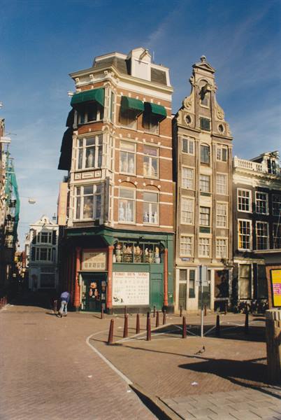 Brick canal houses in Amsterdam, one with ornate gable, under blue sky