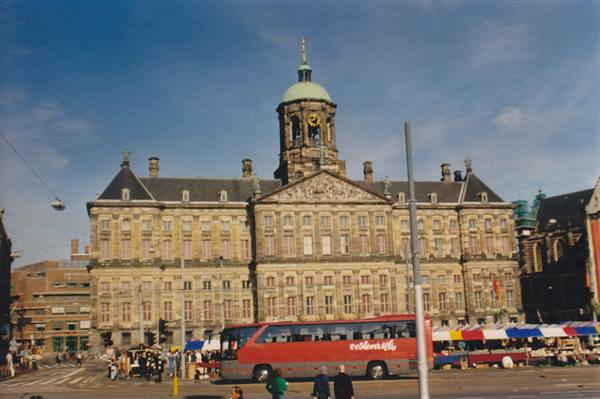 Red bus in front of the Royal Palace of Amsterdam with colorful stalls