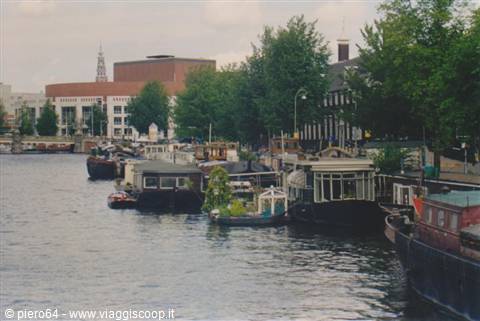 Wooden houseboats moored along an Amsterdam canal among trees