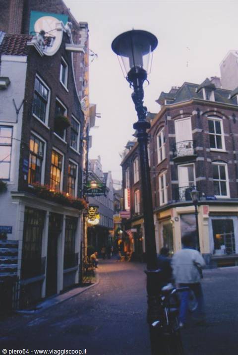 Cast-iron streetlamp in front of brick houses, cyclist passing, Amsterdam