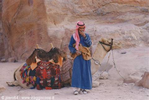 Bedouin in blue robe with saddled camel among Petra sandstone cliffs