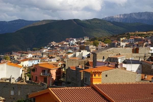 Terracotta rooftops and colorful houses beneath cloudy mountains