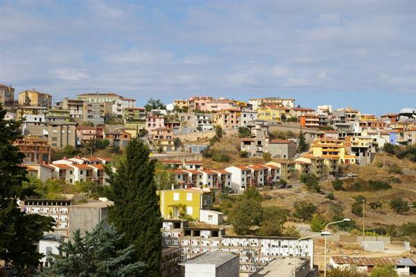 Colorful hillside houses with red roofs among pines under cloudy sky