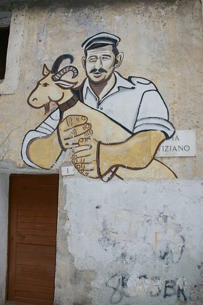 Mural on weathered facade: man in cap holding a goat, beside a wooden door