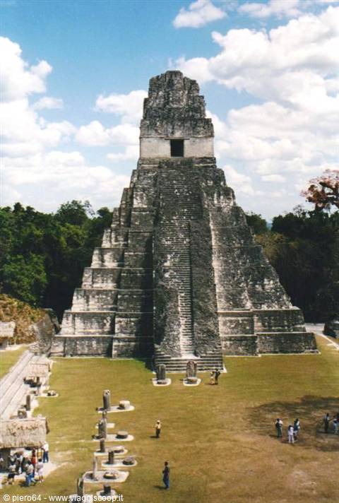 Stone Maya temple with central stairway, grassy plaza and tourists, Tikal