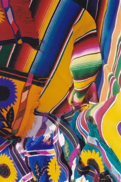 Handwoven blankets in vivid stripes and sunflower patterns piled at a market