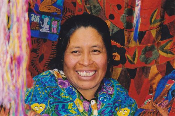 Smiling woman in colorful embroidered blouse among traditional woven textiles at market