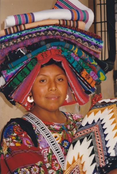 Maya woman balancing colorful woven textiles on her head at the market