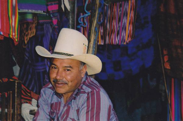 Man in straw hat smiling among colorful hanging fabrics at a market