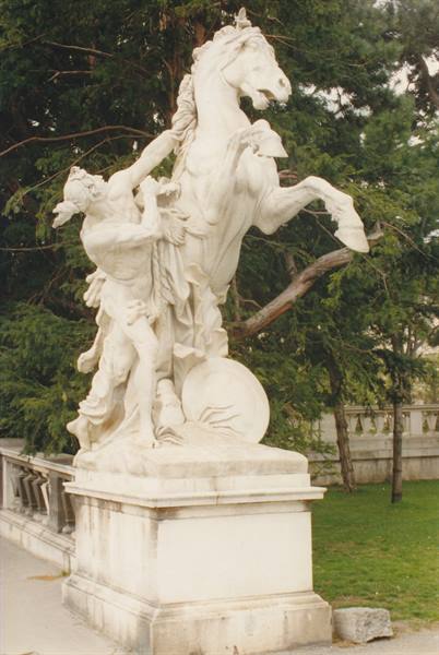 Marble statue of a man taming a rearing horse among green trees