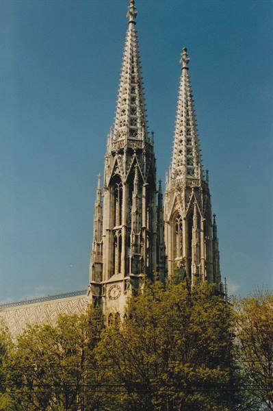 Gothic spires of Vienna's Votivkirche above green trees, blue sky