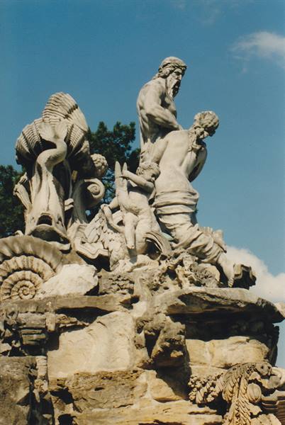 Marble mythological statues on the baroque fountain against a blue sky