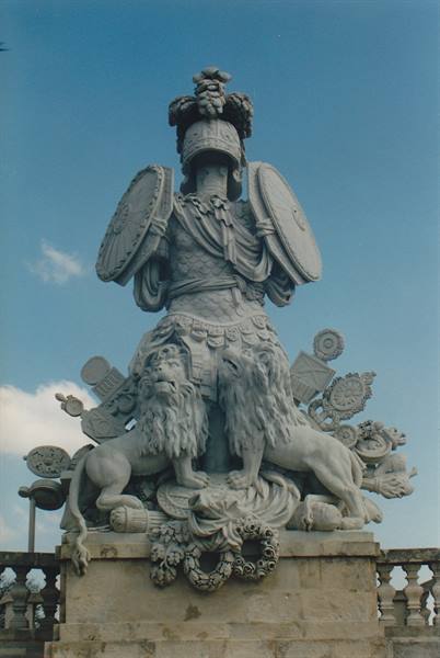Stone sculpture of two lions at the feet of an armored figure against blue sky