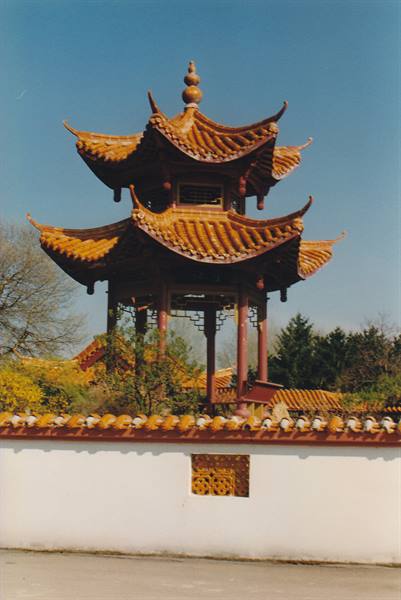 Chinese pavilion with golden curved roofs above white wall, trees and blue sky