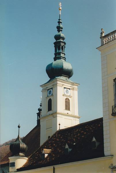 White bell tower with green dome and golden cross, tiled roofs