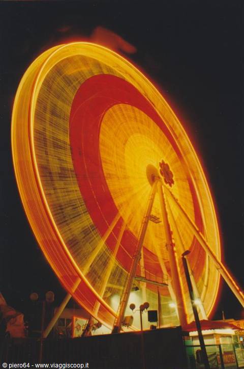 Ferris wheel glowing yellow and red spinning at night fairground