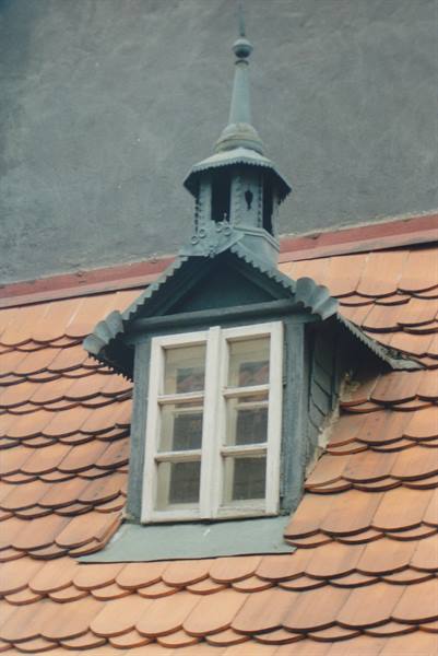 Green dormer window with spire juts from terracotta tile roof