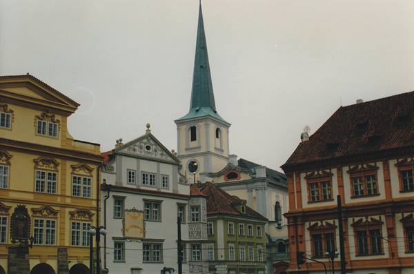 Colorful facades and a green church spire under grey sky, Prague
